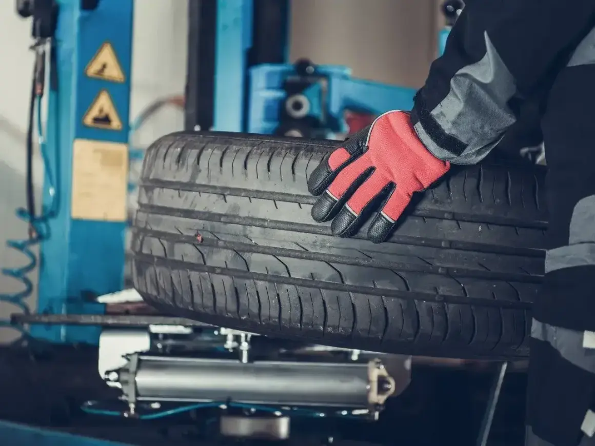 Mechanik w czerwonej rękawicy trzyma oponę. Czy można założyć opony 185 zamiast 195? Sprawdź w serwisie.