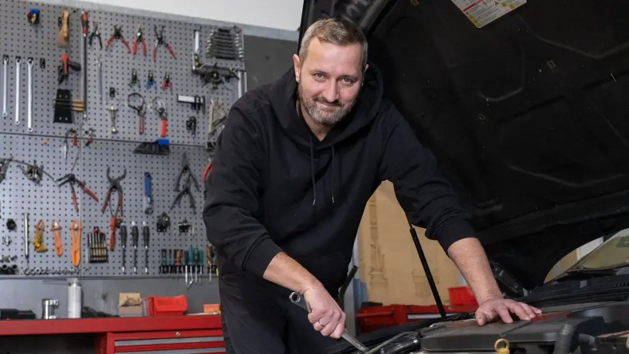 Mechanik w warsztacie, gdzie nawet naprawy nie do naprawy znajdują rozwiązanie. Narzędzia wiszą na ścianie, gotowe do pracy.