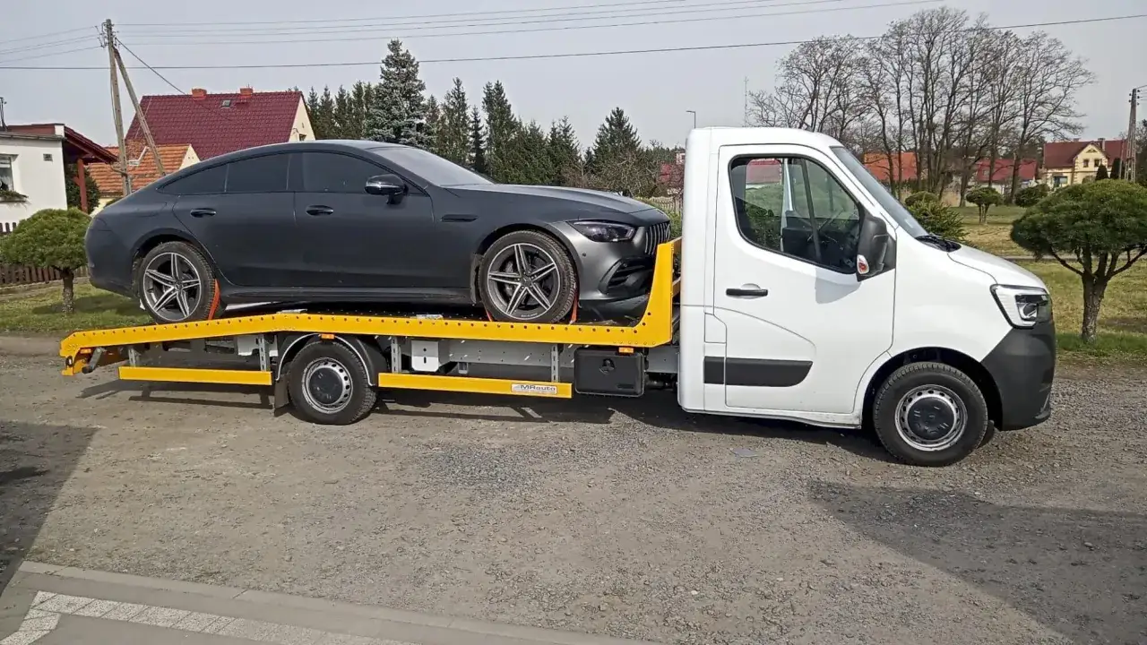 Czarny sportowy samochód na żółtej lawecie, gotowy do transportu tam, gdzie nie można holować.