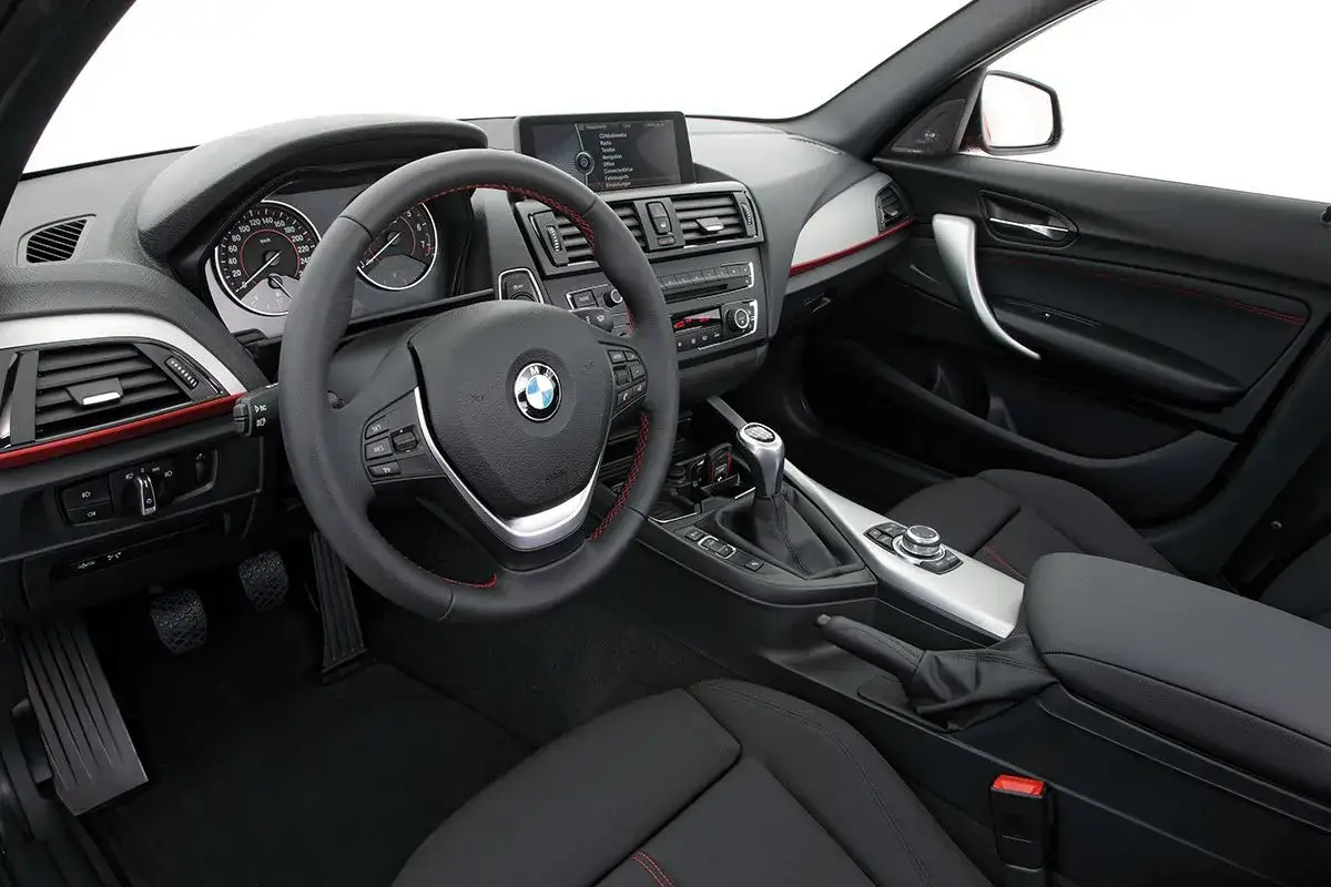 Wnętrze BMW Seria 1. Kierownica, deska rozdzielcza z ekranem i nawiewami, dźwignia zmiany biegów. Opinie o tym modelu są zazwyczaj pozytywne.