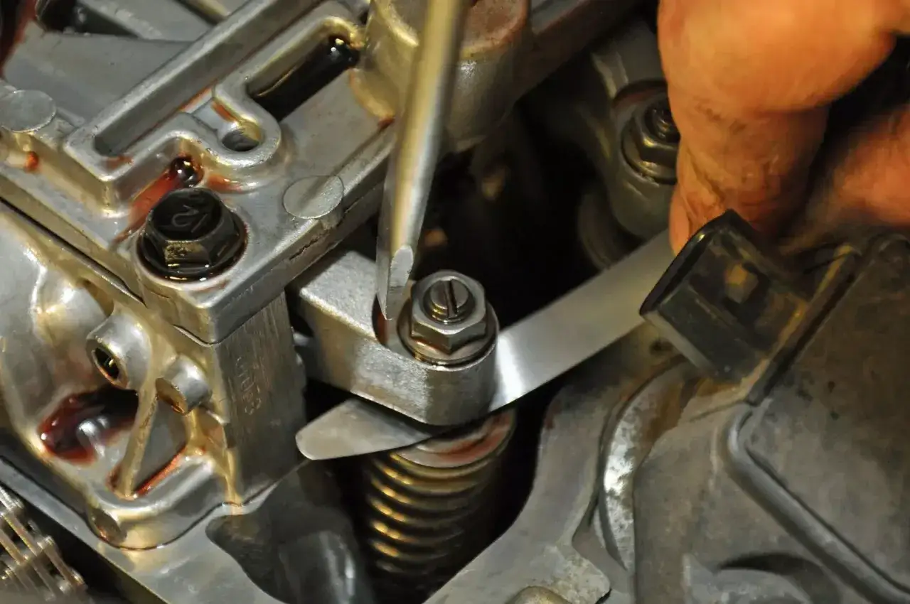 Mechanik reguluje zawory w silniku, używając śrubokręta i cienkiego metalowego narzędzia.