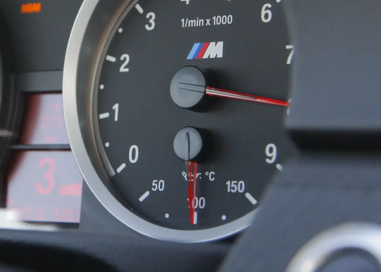 Wskaźnik pokazuje temperaturę oleju w silniku BMW M, wskazówka jest blisko 100°C.