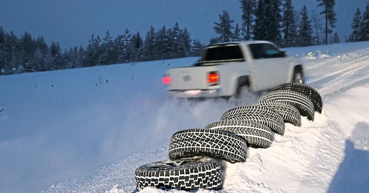 Na śnieżnej drodze, wśród drzew, biały pickup z napędem 4x4 sunfull na zimowych oponach.