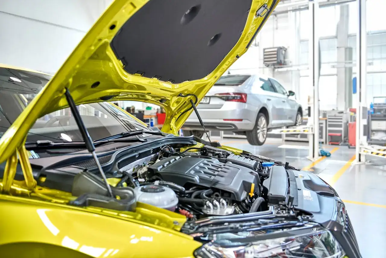Żółty samochód z otwartą maską w warsztacie. Mechanik przygotowuje się do wymiany paska rozrządu, zapewniając płynną pracę silnika.