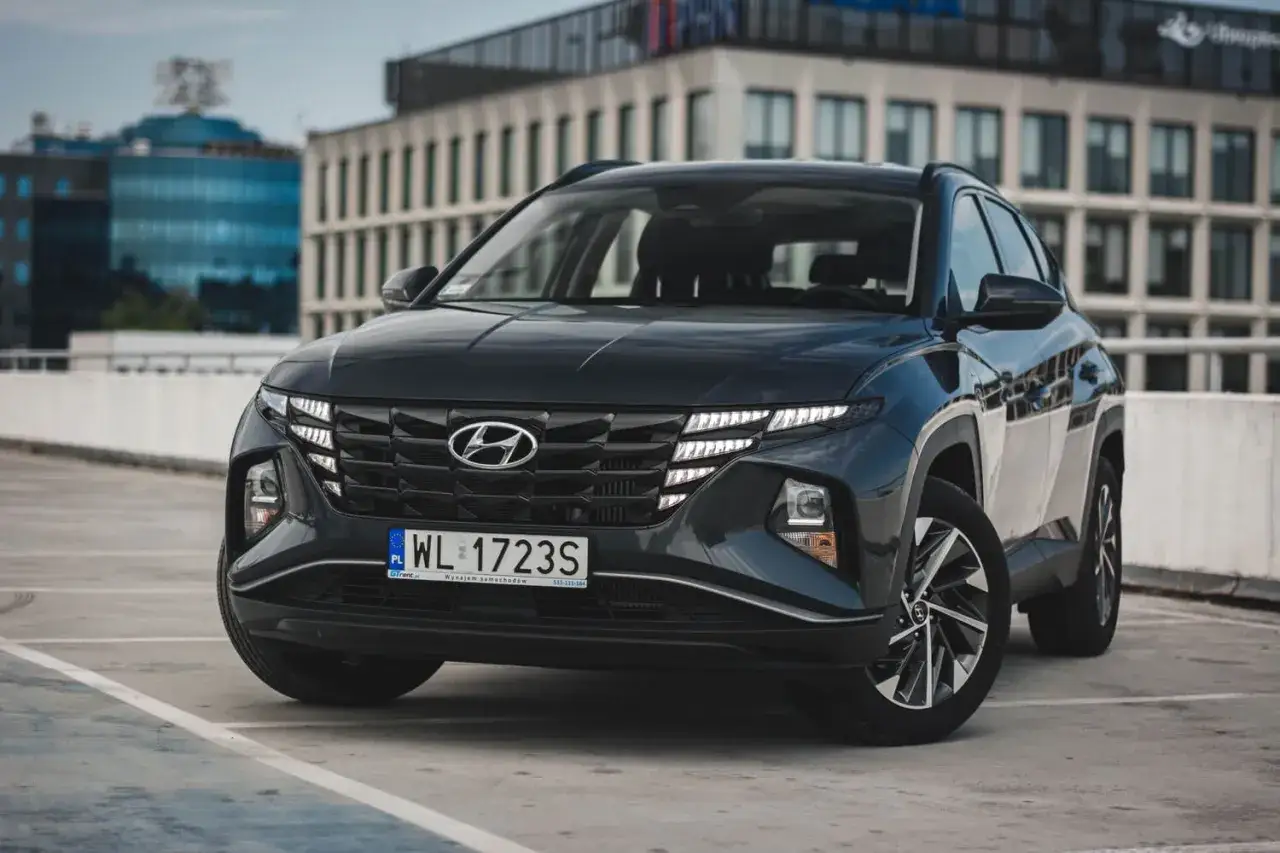Nowoczesny czarny Hyundai Tucson, jeden z wielu modeli tej marki, parkuje przed biurowcem.