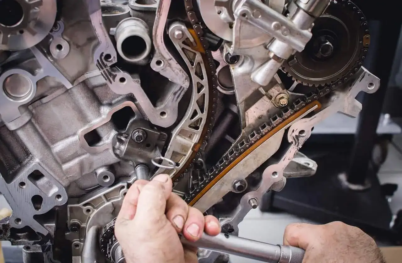 Mechanik pracuje przy rozrządzie silnika. Widoczne elementy to łańcuch rozrządu i koła zębate. Objawy zużycia poduszki silnika mogą być różne.