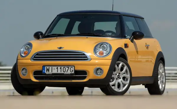 Żółty mini r50 z czarnym dachem i felgami stoi na zewnątrz.
