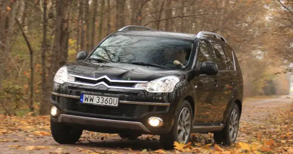 Czarny Citroen C-Crosser jedzie po leśnej drodze pokrytej jesiennymi liśćmi.
