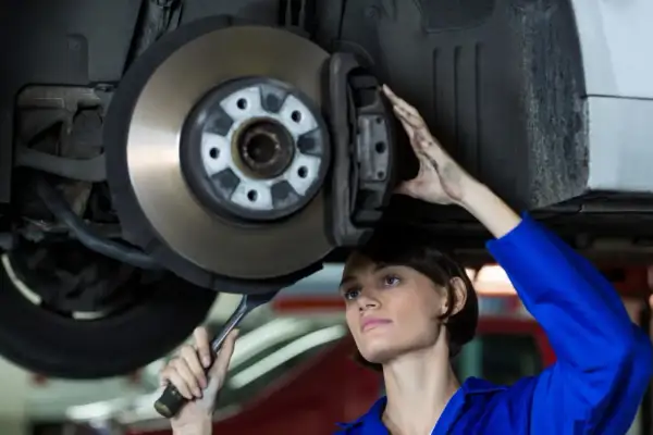 Mechaniczka w niebieskim kombinezonie wykonuje wymianę tarcz hamulcowych, trzymając klucz.