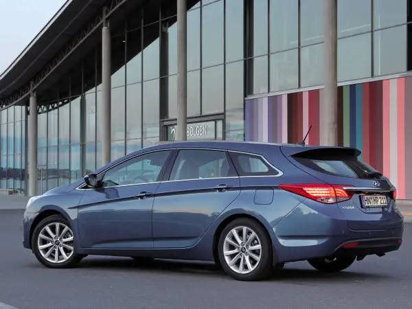 Niebieski Hyundai i40 kombi zaparkowany przed nowoczesnym budynkiem z kolorowymi pasami. Wiele osób chwali ten model, czytając **hyundai i40 opinie**.