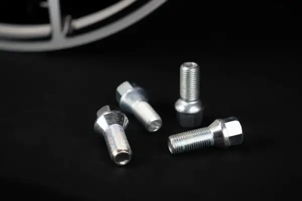 Cztery śruby do felg aluminiowych leżą na czarnym tle. Zastanawiasz się, jakie śruby do felg aluminiowych wybrać?