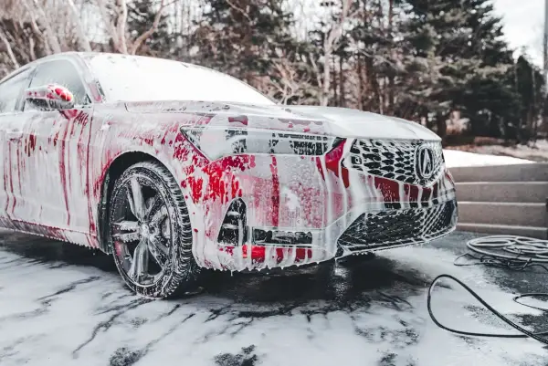 Czerwony samochód pokryty pianą, stojący na śniegu. Czy można myć auto w mrozie? Piana spływa po karoserii, tworząc ciekawe wzory.