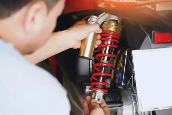 Mechanik dokonuje wymiany amortyzatorów w skuterze, używając złotego narzędzia do regulacji.
