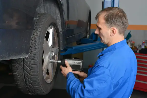 Mechanik w niebieskim kombinezonie dokręca koło kluczem pneumatycznym, dbając o to, z jaką siłą dokręcać koła.