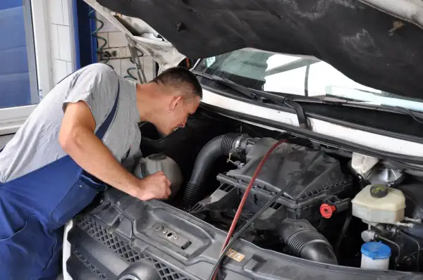 Mechanik w niebieskim ogrodniczkach pochyla się nad silnikiem, przygotowując się do wymiany świec żarowych.