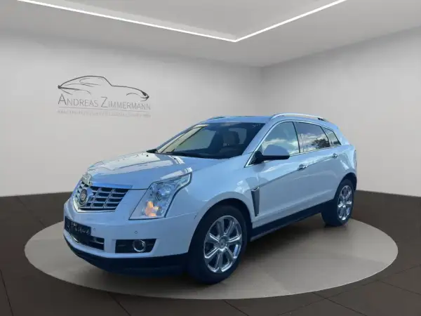 Biały Cadillac SRX z chromowanymi felgami, zaparkowany na obrotowej platformie w salonie samochodowym.