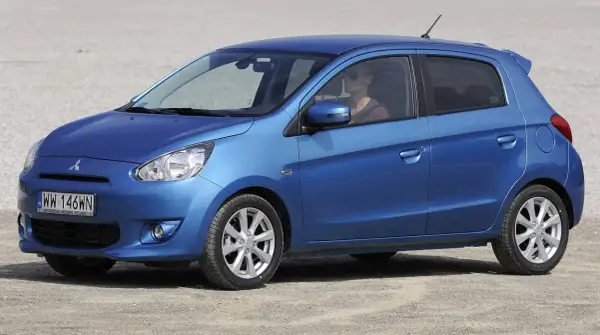 Niebieski Mitsubishi Mirage, idealny dla szukających bezawaryjnych samochodów do 20 tys. zł. Kobieta za kierownicą w okularach przeciwsłonecznych.