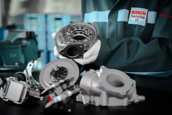 Mechanik w białych rękawiczkach prezentuje części turbosprężarki, sugerując domowe ustawienie sztangi turbiny.