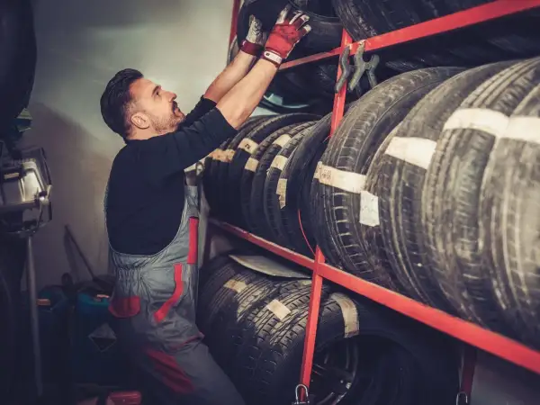 Mechanik w czerwonych rękawicach sięga po oponę Laufenn z regału.