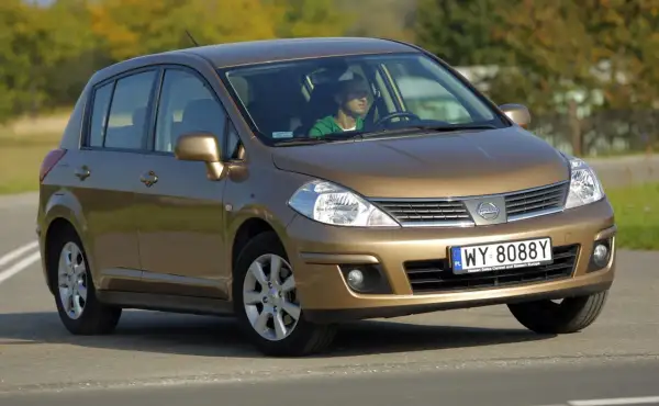 Złoty Nissan Tiida z mężczyzną za kierownicą jedzie po drodze.