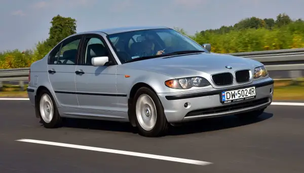 Srebrne BMW E46 330d na drodze. Kierowca w okularach, za nim zielone drzewa. Opinie o tym modelu są zazwyczaj pozytywne.