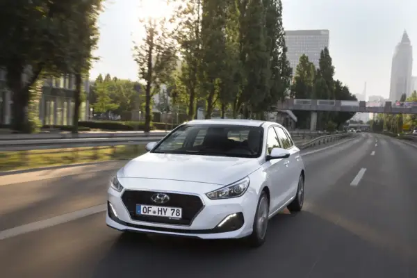 Biały Hyundai i30 1.4 benzyna na drodze. Kierowca w okularach przeciwsłonecznych. Opinie o tym modelu są pozytywne.