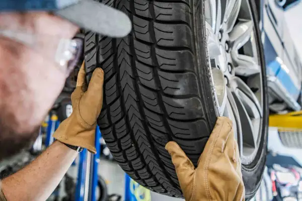 Mechanik w rękawiczkach ogląda bieżnik nowej opony samochodowej.