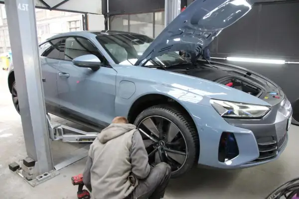 Mechanik pracuje przy podnośniku, wymieniając opony w szarym samochodzie elektrycznym. Szybka wymiana opon to klucz do bezpieczeństwa.