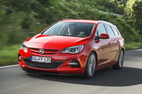 Czerwona Astra J 1.7 CDTI w wersji kombi pędzi po krętej drodze wśród zieleni.