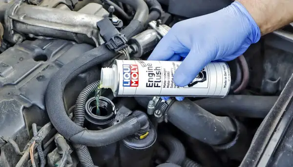 Ręka w niebieskiej rękawiczce wlewa płyn do płukania silnika Liqui Moly. Wiele osób szuka opinii o Ceratec, ale to właśnie ten produkt dba o czystość silnika.