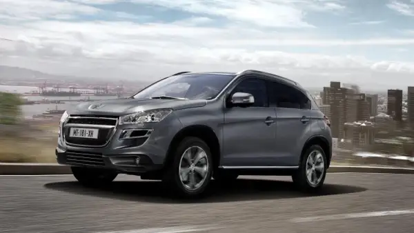 Szary Peugeot 4008 jedzie po drodze z widokiem na miasto i port.