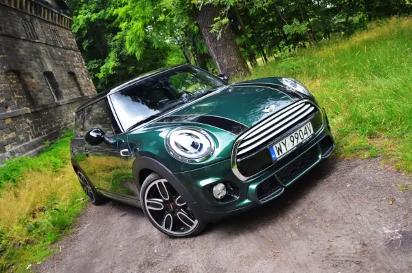 Zielony Mini Cooper na leśnej drodze. Wiele osób chwali sobie ten model, a jego opinie są zazwyczaj pozytywne.