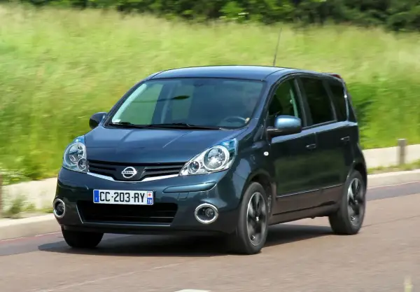 Ciemnozielony Nissan Note E11 w ruchu, z rozmytym tłem zieleni i drogi.
