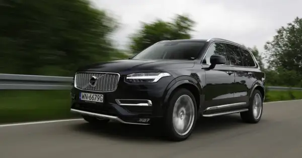 Czarne Volvo XC90 V8 pędzi po drodze, rozmazane drzewa i krajobraz świadczą o dużej prędkości.