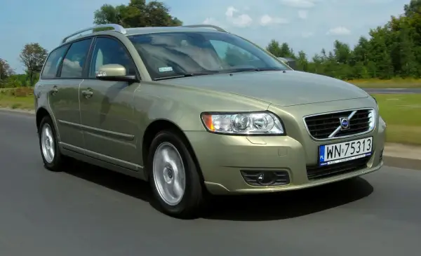Złoty Volvo V50 1.6 diesel w ruchu drogowym, z zielenią drzew w tle.