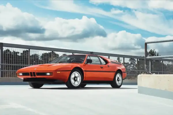 Pomarańczowy klasyk BMW E26 na tle nieba z chmurami.
