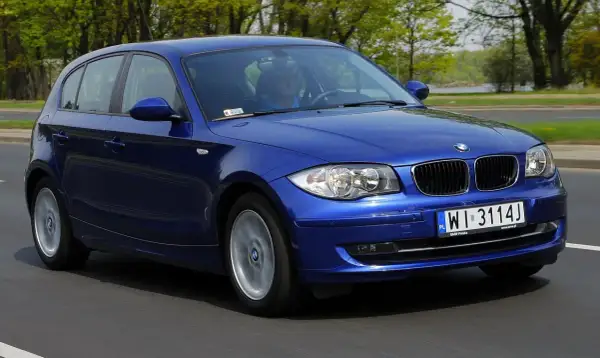 Niebieskie BMW Serii 1 w ruchu drogowym. Kierowca w niebieskiej koszulce. Wiele pozytywnych bmw seria 1 opinie potwierdza jego jakość.