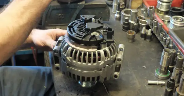 Mechanik sprawdza alternator, zastanawiając się, ile kosztuje regeneracja alternatora. W tle widać narzędzia.