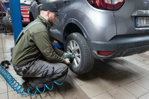 Mechanik w warsztacie dokonuje zmiany opon na zimowe, używając klucza pneumatycznego do odkręcenia śrub w kole samochodu.