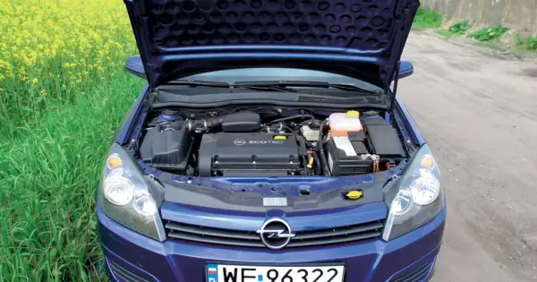 Silnik Ecotec w niebieskim Opel Astra H 1.6 benzyna, z otwartą maską, na tle pola rzepaku.