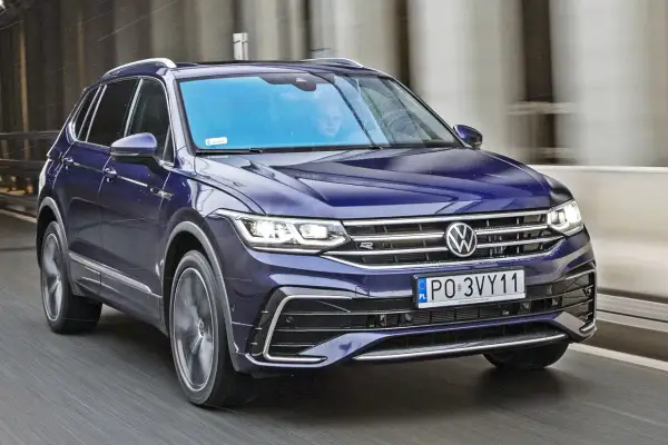 Niebieski Volkswagen Tiguan w ruchu. Kierowca i pasażer widoczni przez przednią szybę. Wiele pozytywnych volkswagen tiguan opinie potwierdza jego wszechstronność.