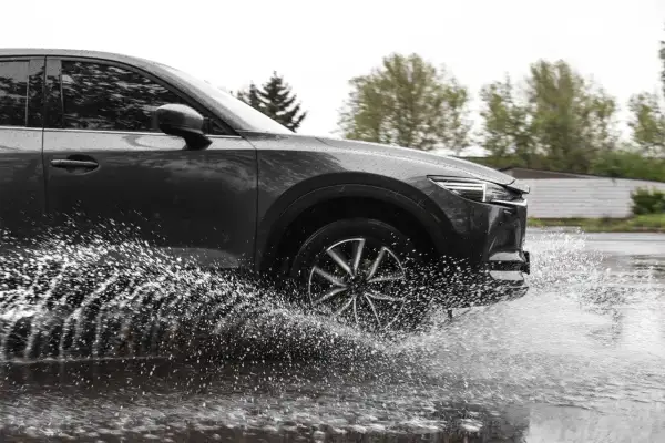 Ciemny samochód na mokrej drodze, koło rozpryskuje wodę, groźny aquaplaning.