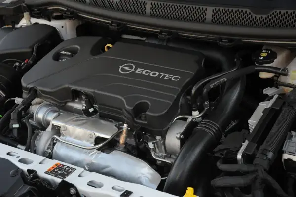Silnik Opel Astra 1.4 Turbo Ecotec. Widoczny turbosprężarka, kolektor dolotowy i osłona silnika.