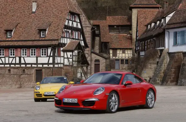 Dwa Porsche, czerwone i żółte, stoją przed zabytkowymi domami. Czy to PDK?