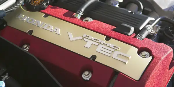 Złota pokrywa zaworów z napisem HONDA VTEC w czerwonej obudowie silnika.