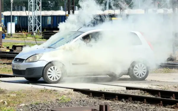 Srebrny Ford Fiesta z silnikiem diesla w obłokach dymu, na tle torów kolejowych.