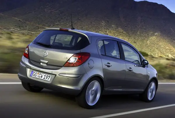 Szary Opel Corsa D 1.2 benzyna w ruchu, z widokiem na tył, na tle górskiego krajobrazu.