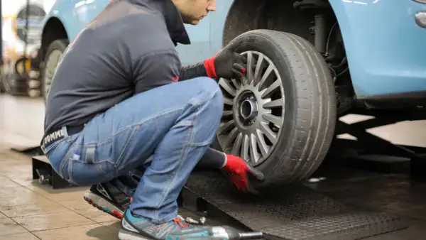Mechanik w rękawiczkach sprawdza oponę samochodu na podnośniku.