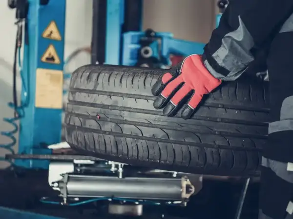 Mechanik w czerwonej rękawicy trzyma oponę. Czy można założyć opony 185 zamiast 195? Sprawdź w serwisie.