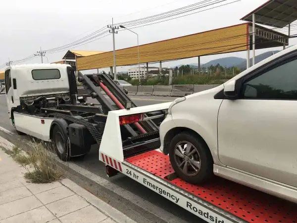 Pomoc drogowa w akcji: białe auto jest ładowane na lawetę. Widać, jak holować auto, gdy jest potrzebna pomoc.